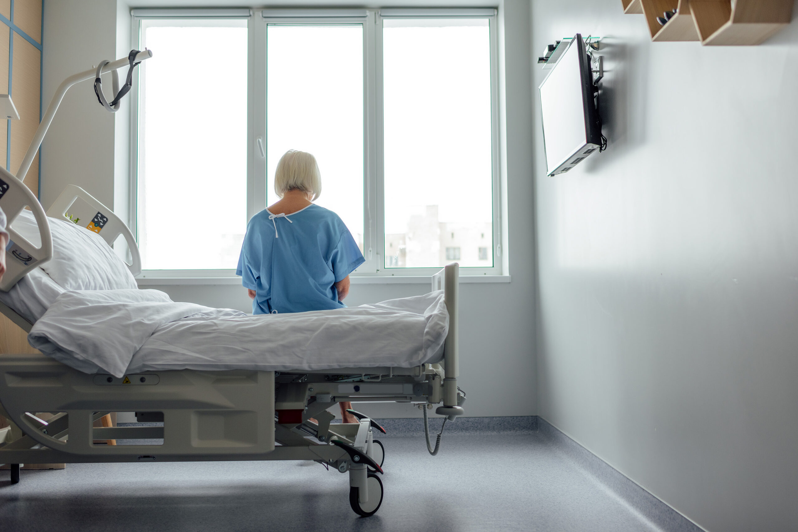 back view of lonely senior woman sitting on bed in hospital ward